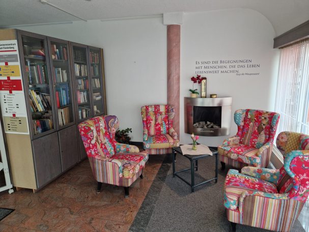 Bunte Sessel um einen kleinen Tisch vor einer Bibliothek und neben einem gemütlichen Kamin.