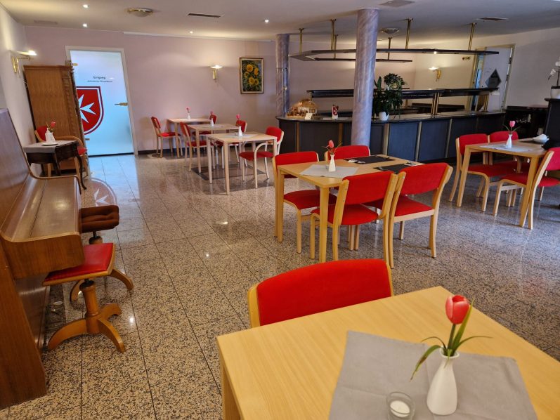 Helle, moderne Restaurant-Interieur mit roten Stühlen und Tischen sowie Blumen auf den Tischen und einem Klavier auf der Seite.