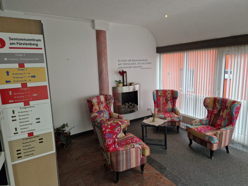 Gemütliches Kaminzimmer mit bunten Sesseln und einem Tisch vor einer Bibliothek.