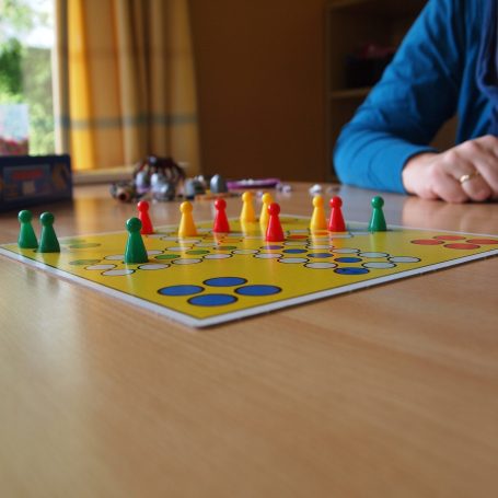 Ein Brettspiel mit bunten Spielfiguren auf einem Tisch an welchem Senioren spielen.