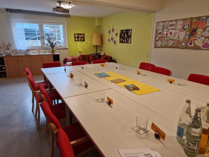 Cafe Malta und Spieleraum mit einem großen Tisch, roten Stühlen und einer bunten Wanddekoration.