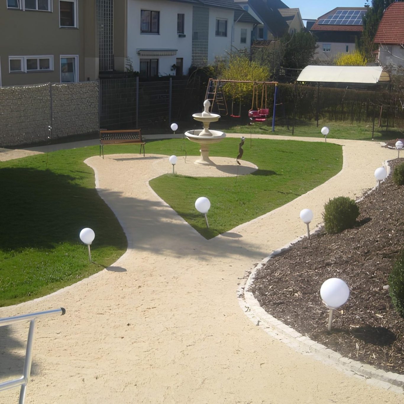 Garten mit Rasen, Pflanzen mit Springbrunnen und einer weißen Kugelbeleuchtung entlang der Wege.