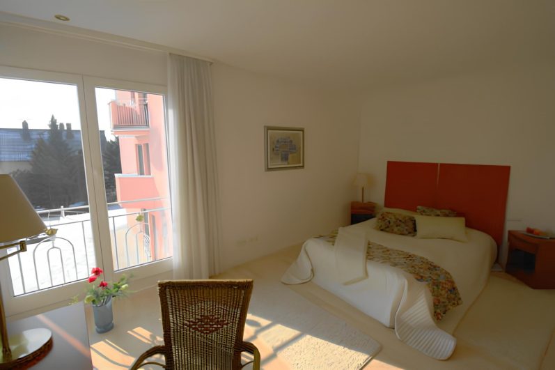 Helles Schlafzimmer mit einem Bett, Stuhl und Blick auf einen Balkon.