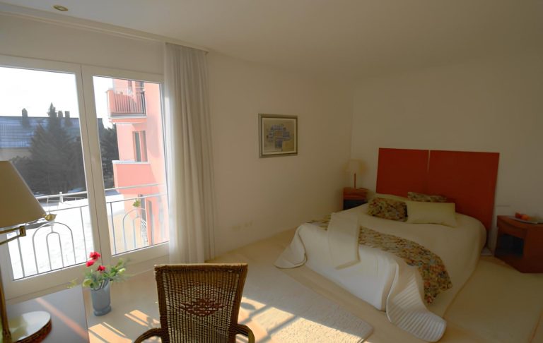 Helles Schlafzimmer mit einem Bett, Stuhl und Blick auf einen Balkon.