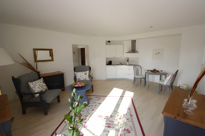 Helles, moderne Wohnzimmer mit Sesseln, Tisch und offener Küche.