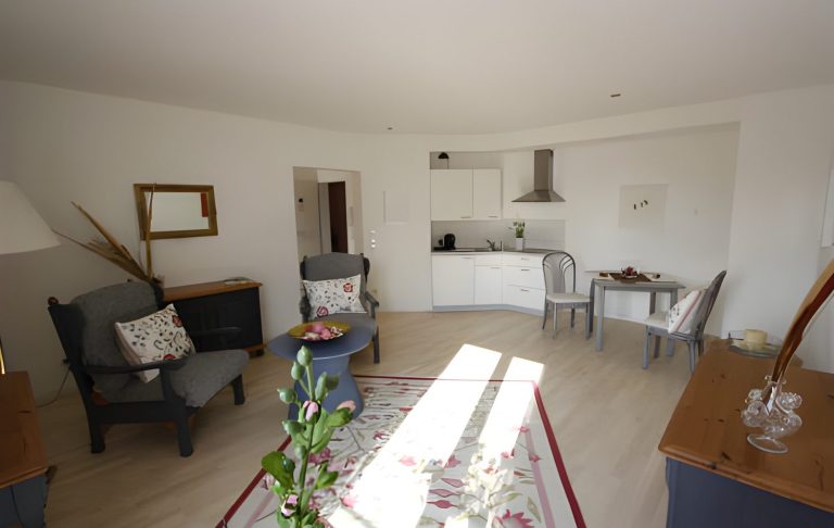 Helles, moderne Wohnzimmer mit Sesseln, Tisch und offener Küche.