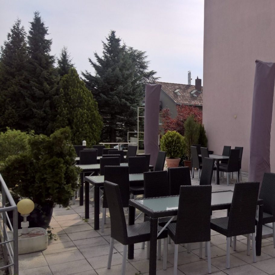 Schöne Terrasse mit Tischen und Stühlen, umgeben von Bäumen und Pflanzen.